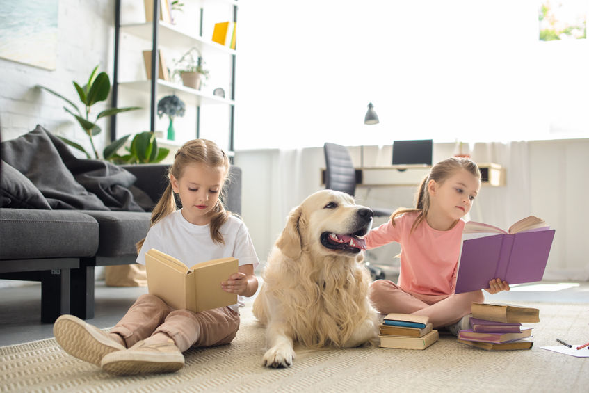 cute little sisters reading books with golden retriever dog near by at home